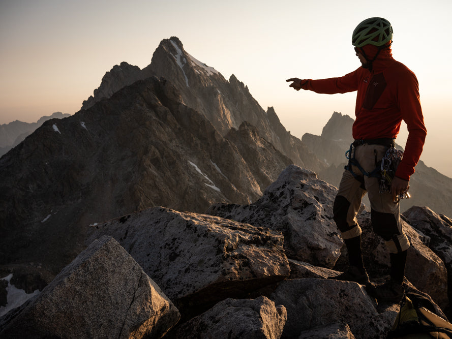 Climber on the South Teton at sunrise pointing back along the Grand Traverse ridgeline toward the Grand Teton