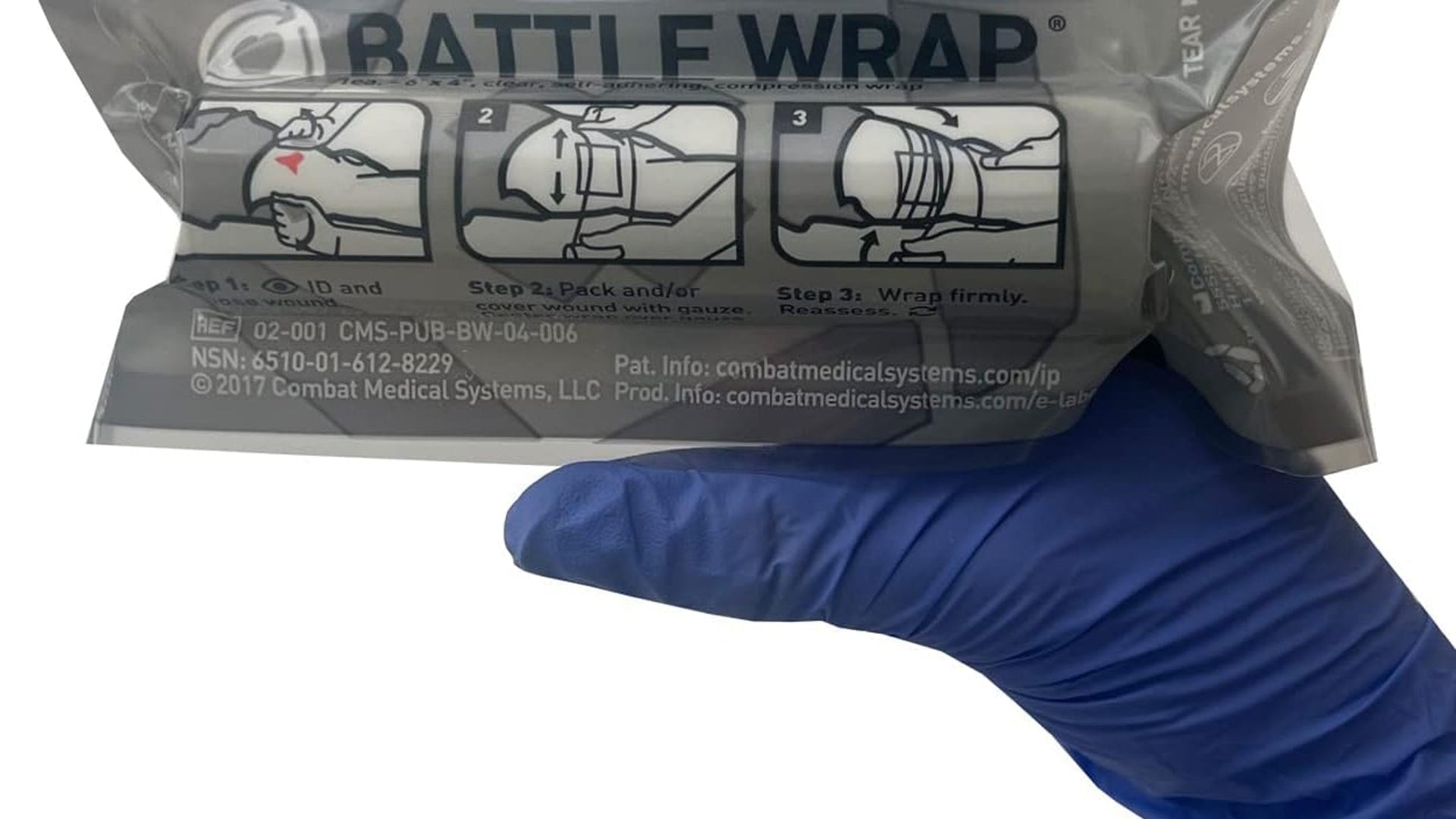 Gloved hand holding a sealed Battle Wrap transparent compression dressing with printed application steps