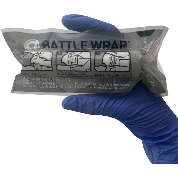 Gloved hand holding a sealed Battle Wrap transparent compression dressing with printed application steps