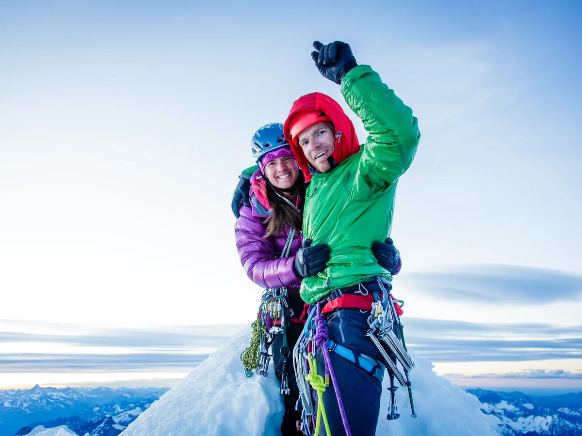 A climbing couple in puffy jackets celebrating together on a snowy summit above the clouds