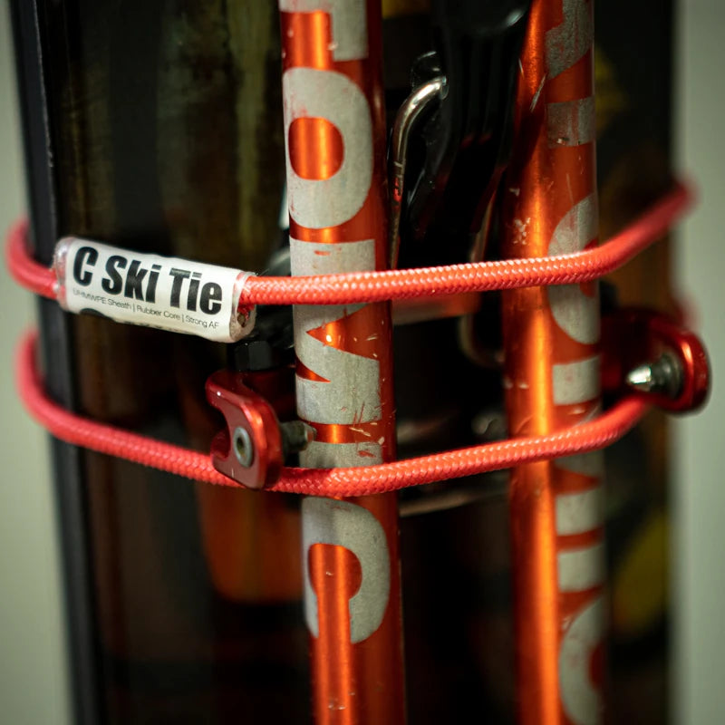Red C Ski Tie wrapped around a bundled pair of skis and poles, holding them tight for the boot pack