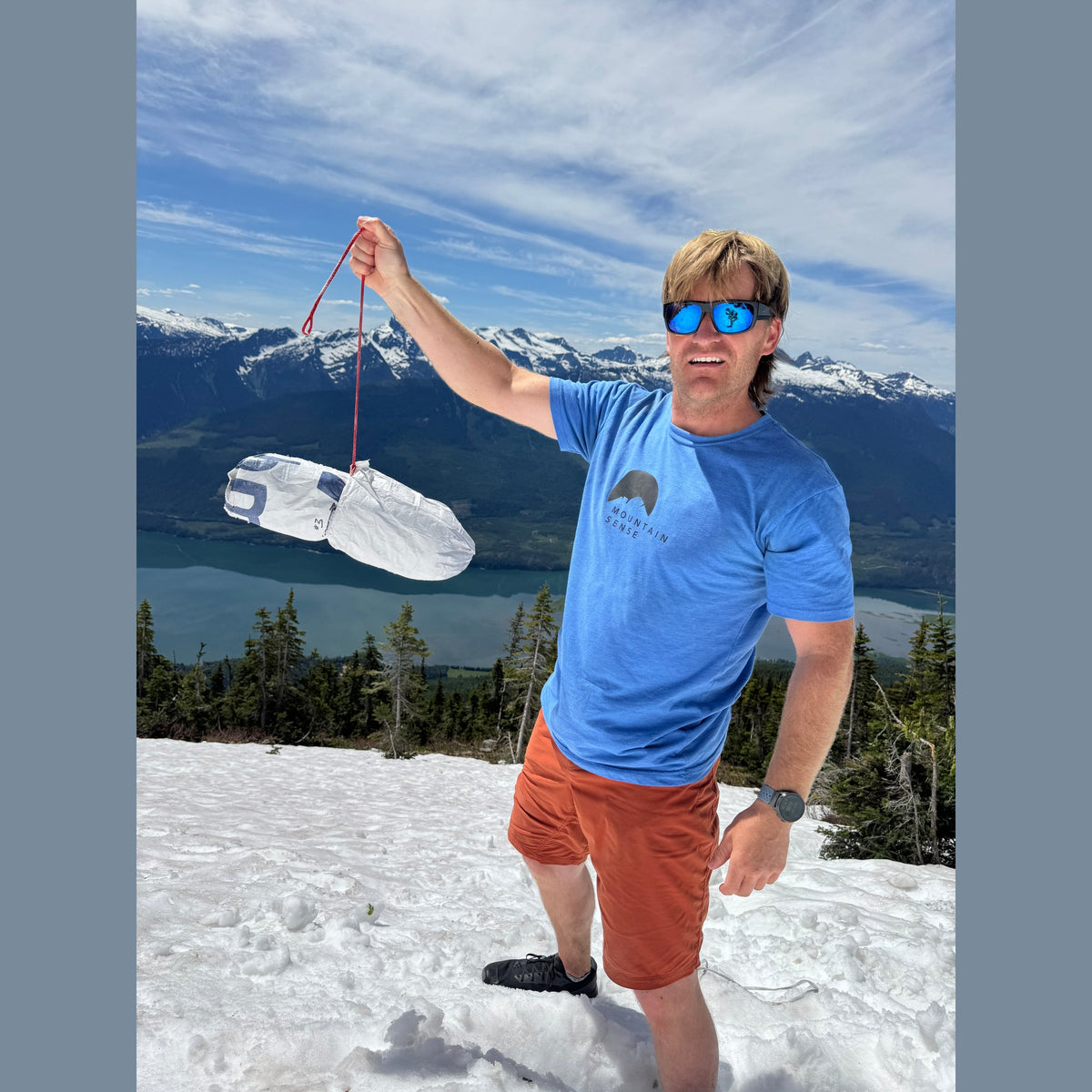 Mark Smiley holding the white Tyvek T-Trench Stuff Sack on a spring snowfield above a mountain lake