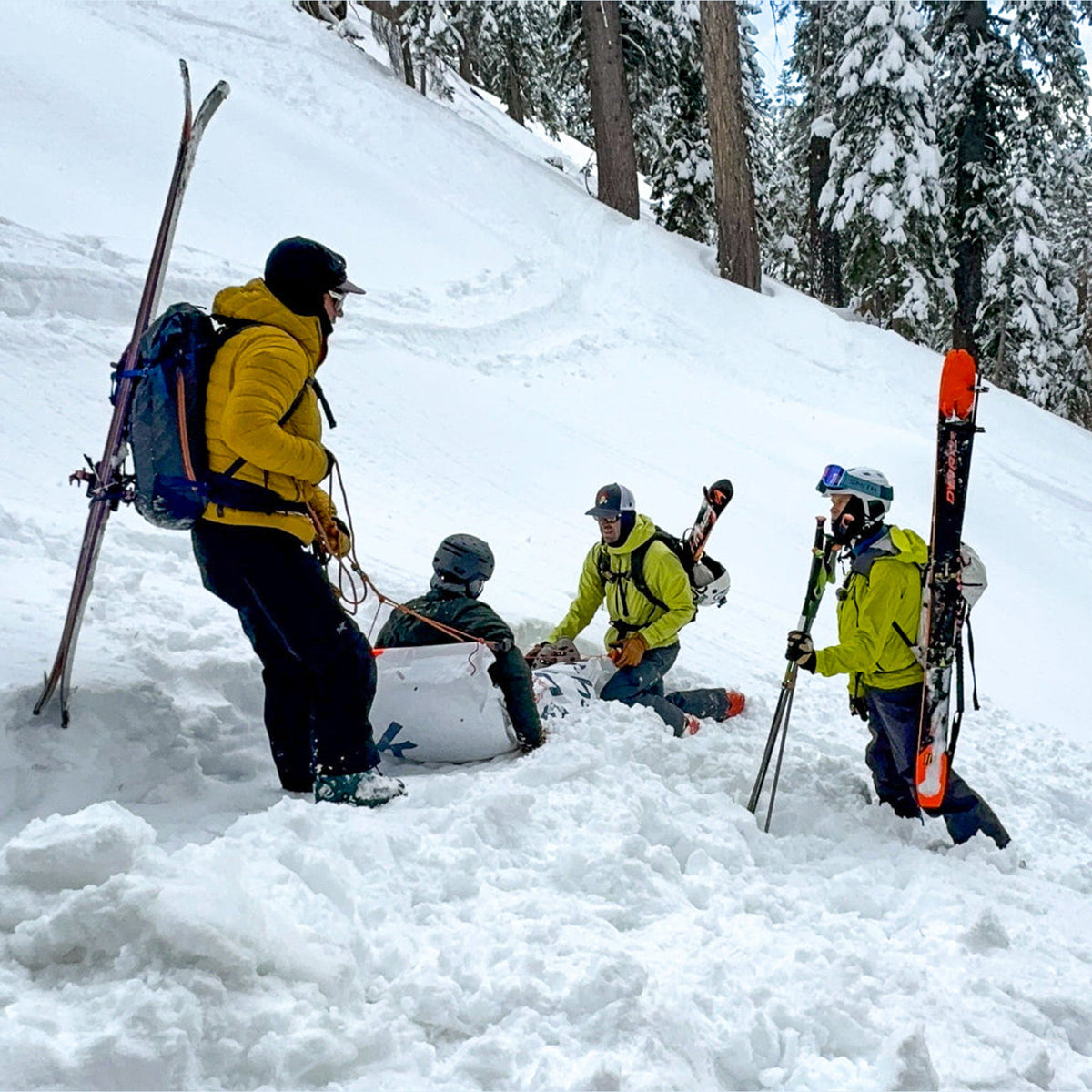Real backcountry rescue in progress: three skiers assist an injured partner sitting in the snow below snowy trees